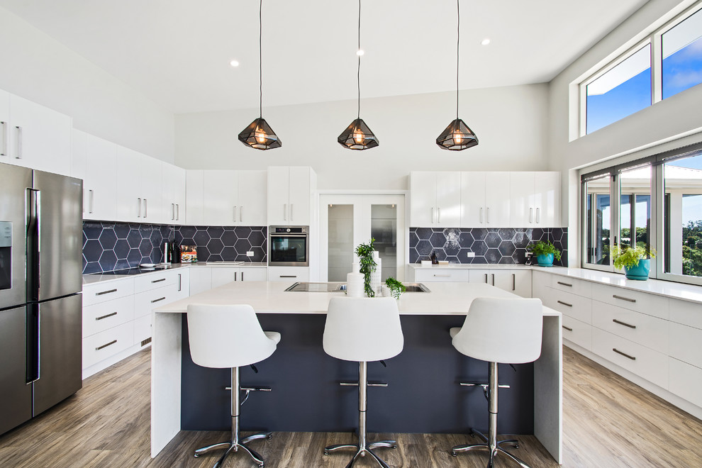 This is an example of a large transitional u-shaped open plan kitchen in Other with a double-bowl sink, flat-panel cabinets, white cabinets, blue splashback, ceramic splashback, stainless steel appliances, light hardwood floors, with island and brown floor.