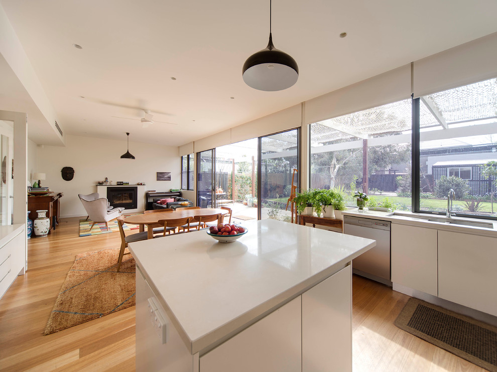 Mid-sized contemporary u-shaped eat-in kitchen in Melbourne with an undermount sink, flat-panel cabinets, white cabinets, quartz benchtops, white splashback, glass sheet splashback, black appliances, light hardwood floors and with island.