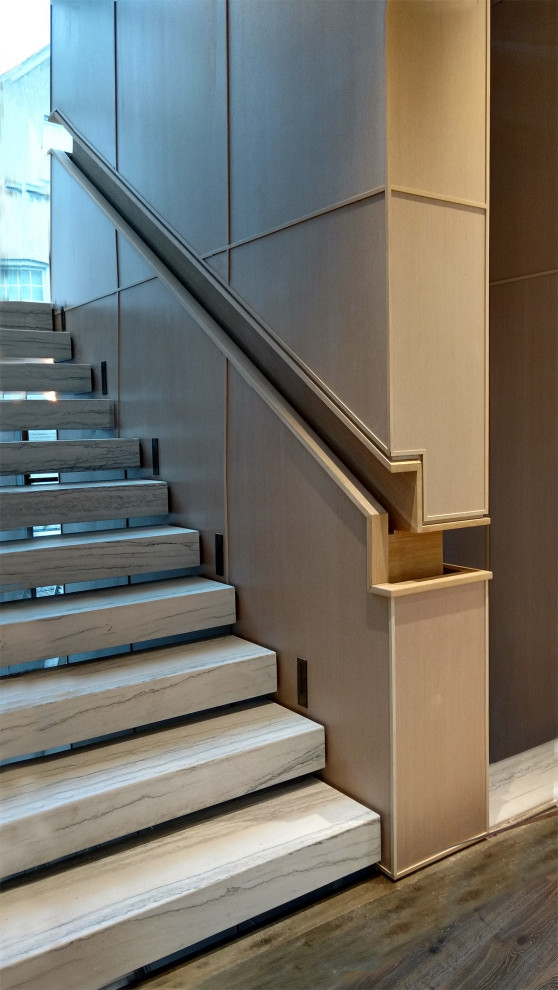 ラグジュアリーなモダンスタイルのおしゃれな階段 (大理石の蹴込み板、木材の手すり、パネル壁) の写真
