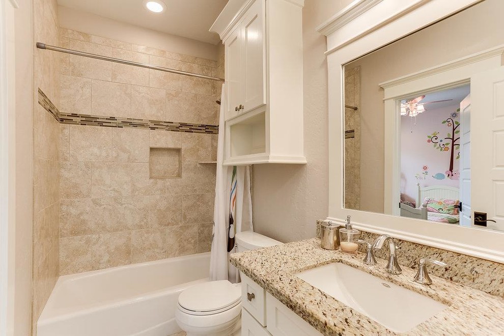 This is an example of a mid-sized arts and crafts kids bathroom in Houston with shaker cabinets, white cabinets, a shower/bathtub combo, a two-piece toilet, beige tile, travertine, beige walls, ceramic floors, an undermount sink, granite benchtops, beige floor and a shower curtain.