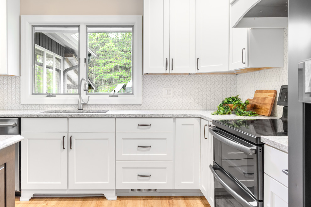 Transitional l-shaped kitchen photo in Minneapolis with an undermount sink, shaker cabinets, white cabinets, granite countertops, white backsplash, ceramic backsplash, stainless steel appliances, an island and gray countertops
