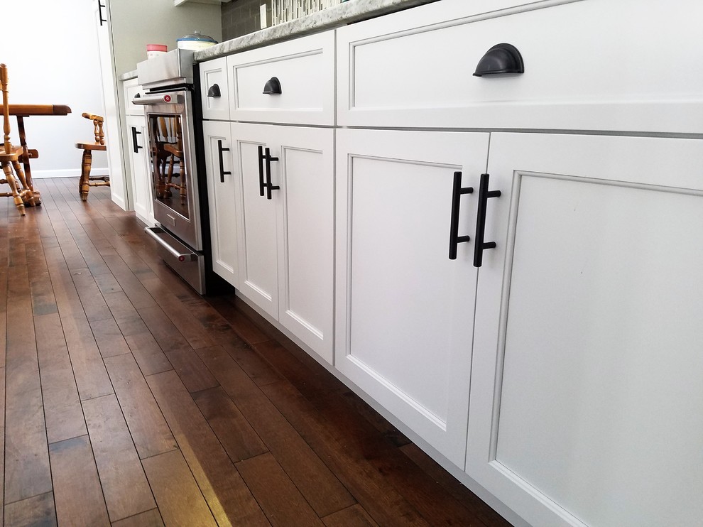 Photo of a large transitional galley open plan kitchen in Bridgeport with an undermount sink, raised-panel cabinets, white cabinets, granite benchtops, brown splashback, ceramic splashback, stainless steel appliances, medium hardwood floors, with island and brown floor.