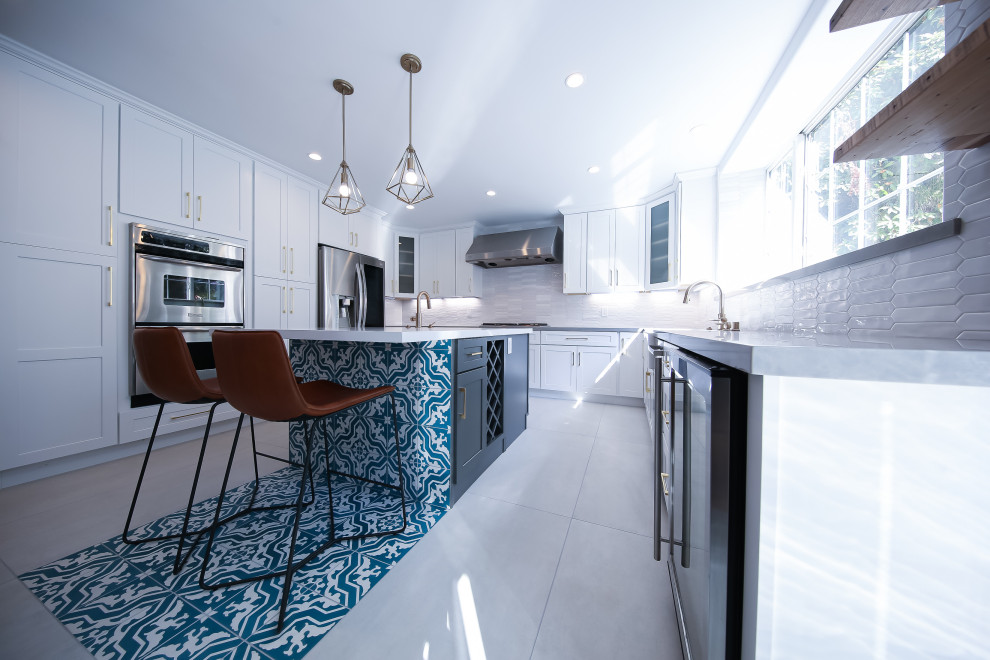 This is an example of a large modern u-shaped eat-in kitchen in Los Angeles with a double-bowl sink, shaker cabinets, white cabinets, quartzite benchtops, white splashback, porcelain splashback, stainless steel appliances, light hardwood floors, with island, brown floor and white benchtop.