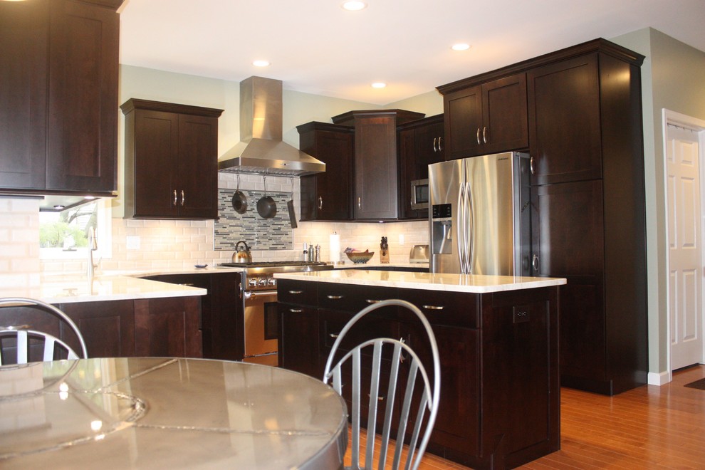 Example of a mid-sized minimalist u-shaped medium tone wood floor kitchen design with shaker cabinets, dark wood cabinets, white backsplash, stainless steel appliances and an island