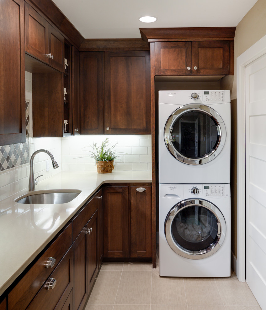 Design ideas for a mid-sized traditional l-shaped dedicated laundry room in Portland with dark wood cabinets, beige floor, white benchtop, an undermount sink, shaker cabinets, quartz benchtops, beige walls, ceramic floors and a stacked washer and dryer.