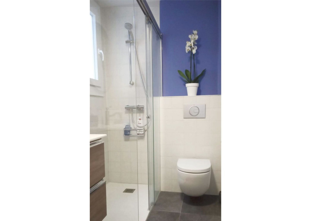Photo of a small modern master bathroom in Other with white cabinets, a curbless shower, a wall-mount toilet, white tile, blue walls, a sliding shower screen, a single vanity and a floating vanity.