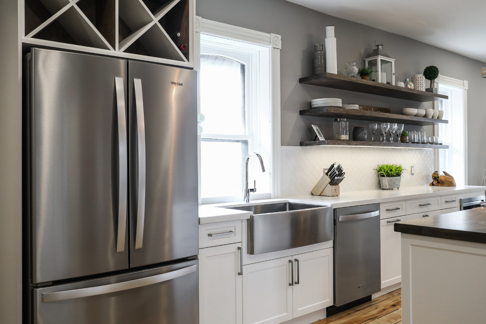 Mid-sized transitional single-wall medium tone wood floor and brown floor eat-in kitchen photo with a farmhouse sink, shaker cabinets, white cabinets, white backsplash, stainless steel appliances, an island and white countertops