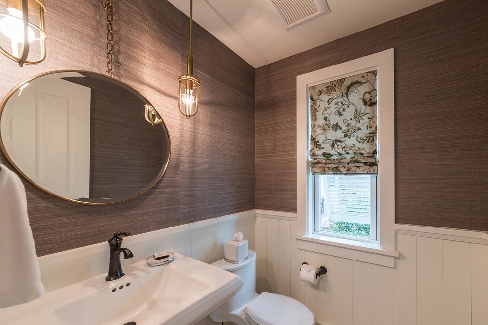 This is an example of a mid-sized beach style powder room in Atlanta with a one-piece toilet, brown walls, light hardwood floors, a pedestal sink and brown floor.