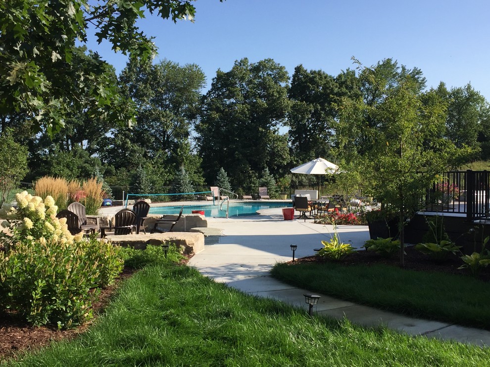 This is an example of a large modern backyard custom-shaped natural pool in Detroit with natural stone pavers and a hot tub.