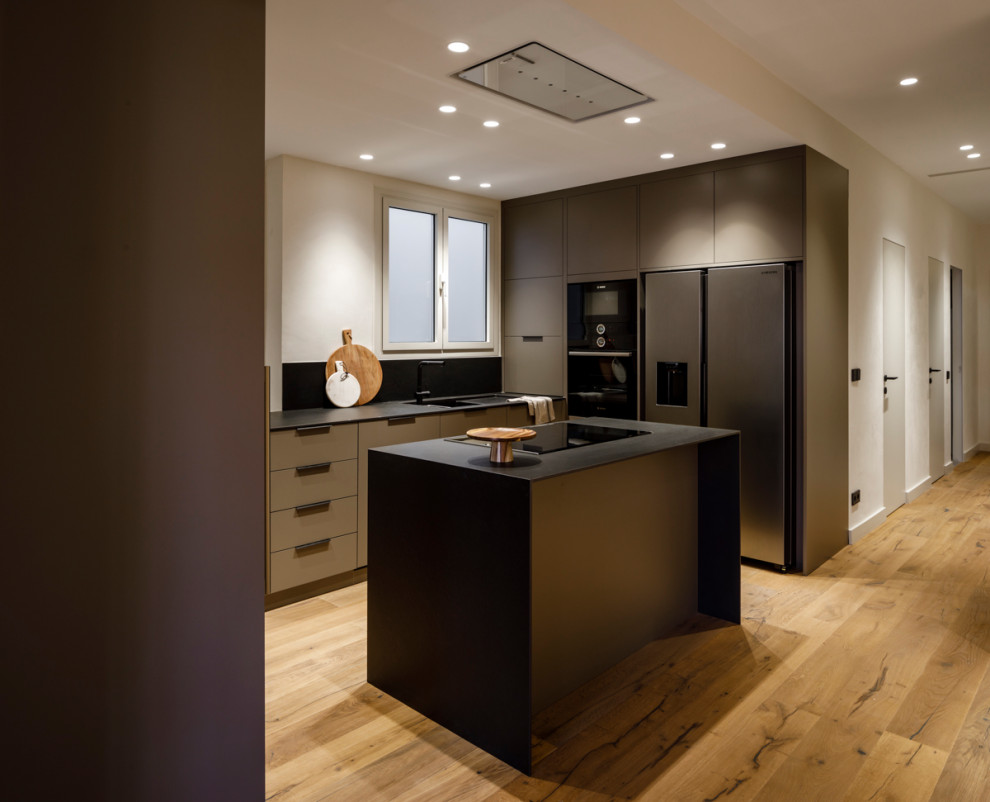 Inspiration for a large modern u-shaped eat-in kitchen in Barcelona with an integrated sink, flat-panel cabinets, black cabinets, marble benchtops, black splashback, marble splashback, black appliances, laminate floors, with island, brown floor and black benchtop.