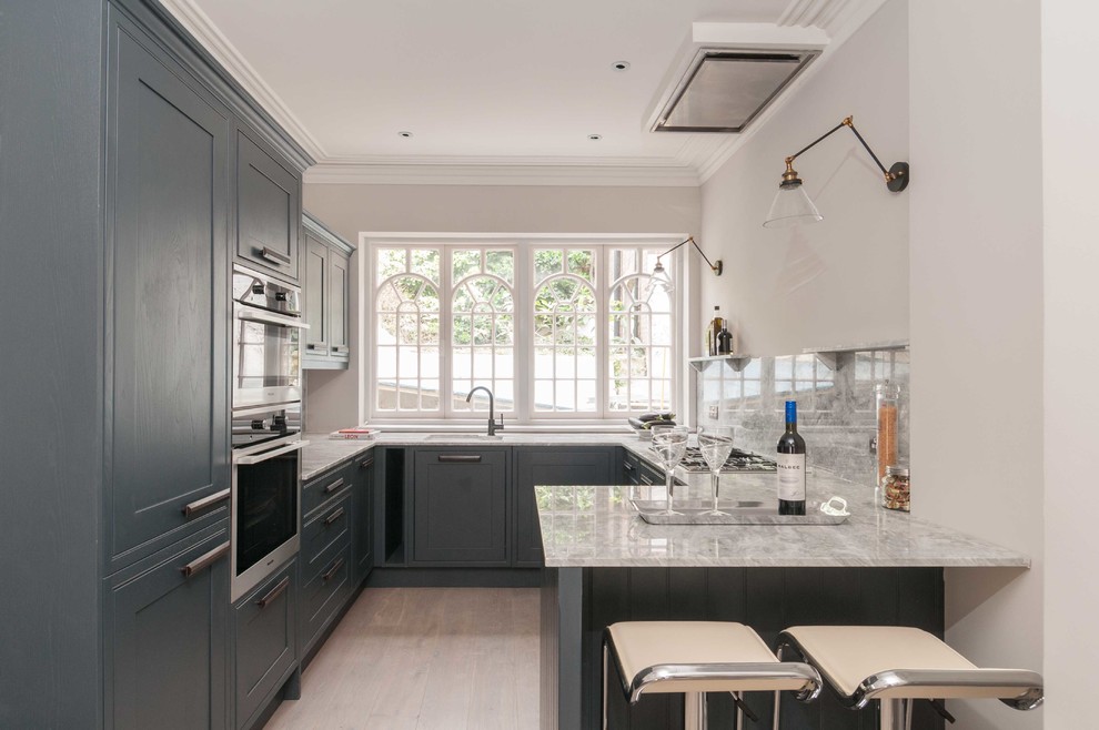 Mid-sized transitional u-shaped eat-in kitchen in London with a drop-in sink, shaker cabinets, grey cabinets, quartzite benchtops, white splashback, stone slab splashback, stainless steel appliances and light hardwood floors.