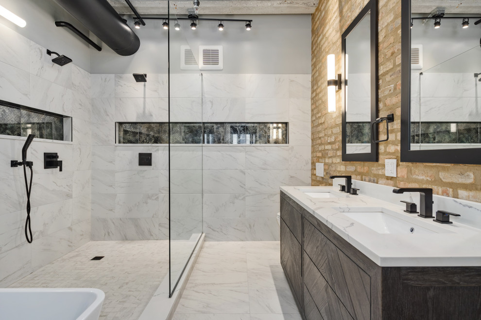 This is an example of a large industrial master bathroom in Chicago with furniture-like cabinets, black cabinets, a freestanding tub, an open shower, a wall-mount toilet, gray tile, porcelain tile, brown walls, porcelain floors, an undermount sink, quartzite benchtops, grey floor, an open shower, white benchtops, a niche, a double vanity, a freestanding vanity, exposed beam and brick walls.