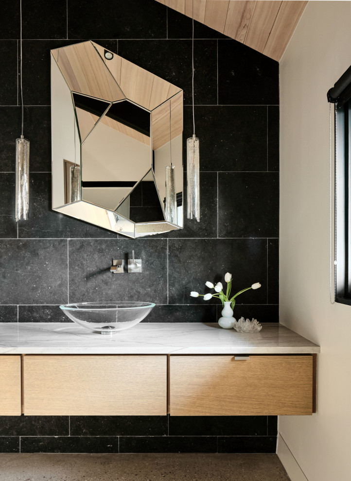 Inspiration for a mid-sized contemporary powder room in Austin with flat-panel cabinets, light wood cabinets, black tile, limestone, black walls, concrete floors, a vessel sink, quartzite benchtops, grey floor, white benchtops, a floating vanity and wood.