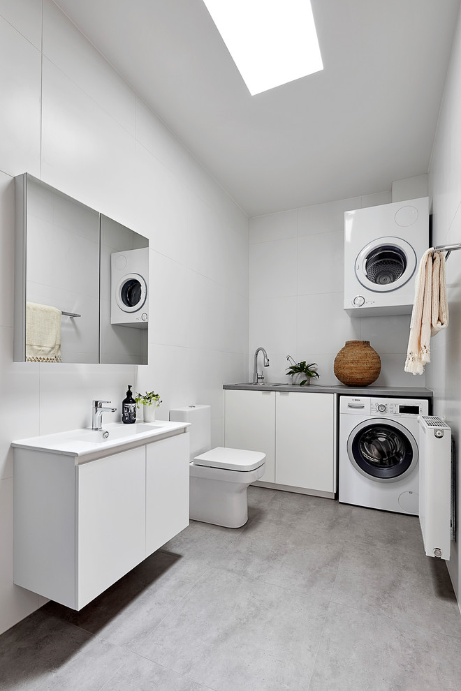 Inspiration for a mid-sized contemporary u-shaped dedicated laundry room in Melbourne with a single-bowl sink, white cabinets, concrete benchtops, white splashback, porcelain splashback, white walls, light hardwood floors, a stacked washer and dryer, brown floor, grey benchtop, coffered and decorative wall panelling.