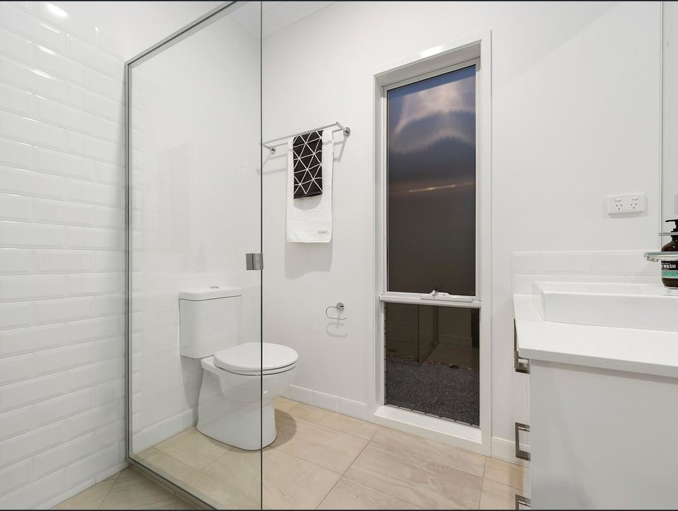 Photo of a mid-sized contemporary 3/4 bathroom in Brisbane with flat-panel cabinets, white cabinets, a drop-in tub, a corner shower, a two-piece toilet, white tile, ceramic tile, white walls, ceramic floors, a vessel sink and engineered quartz benchtops.