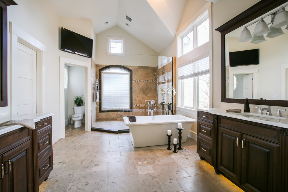 Photo of an expansive contemporary master bathroom in Cedar Rapids with raised-panel cabinets, dark wood cabinets, a freestanding tub, a double shower, beige tile, porcelain floors, an undermount sink, engineered quartz benchtops, a one-piece toilet, a single vanity, beige floor, white benchtops, vaulted, a freestanding vanity, porcelain tile and beige walls.