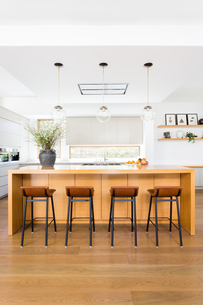 Inspiration for a large contemporary l-shaped kitchen in Los Angeles with flat-panel cabinets, grey cabinets, wood benchtops, white splashback, window splashback, stainless steel appliances, medium hardwood floors, with island, brown floor, brown benchtop and an undermount sink.