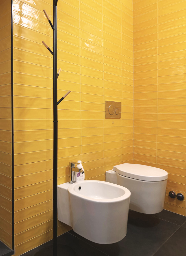This is an example of a small modern 3/4 bathroom in Milan with open cabinets, black cabinets, an alcove shower, a bidet, yellow tile, ceramic tile, white walls, porcelain floors, a console sink, engineered quartz benchtops, black floor, a hinged shower door and black benchtops.