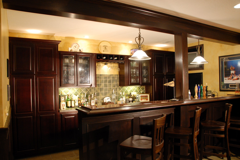 Inspiration for a large traditional galley seated home bar in Columbus with a drop-in sink, raised-panel cabinets, dark wood cabinets, wood benchtops, green splashback, ceramic splashback, ceramic floors, beige floor and brown benchtop.
