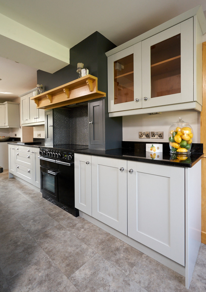 Large traditional l-shaped open plan kitchen in Cheshire with a drop-in sink, shaker cabinets, grey cabinets, granite benchtops, black splashback, granite splashback, panelled appliances, terra-cotta floors, with island, beige floor and black benchtop.