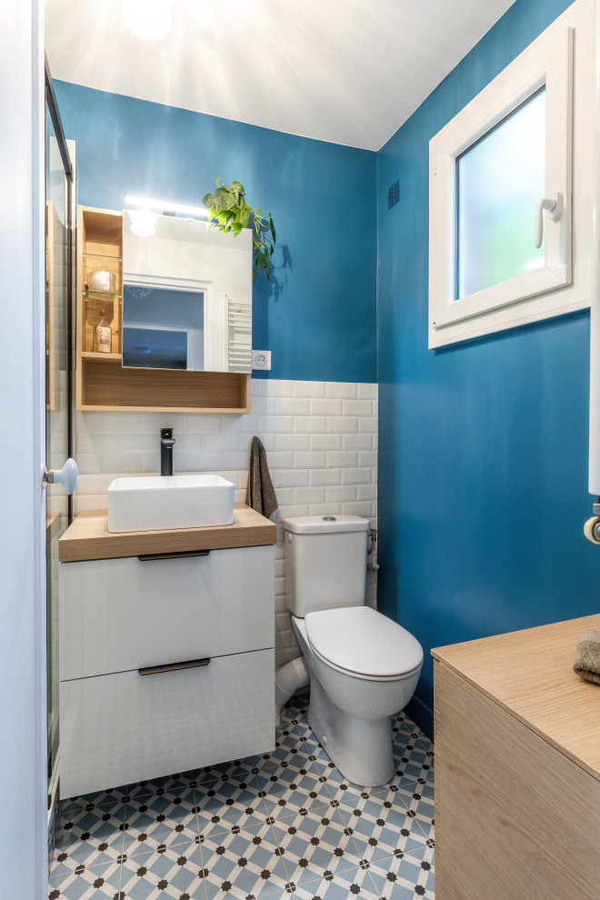 This is an example of a small contemporary master bathroom in Paris with beaded inset cabinets, light wood cabinets, an open shower, a one-piece toilet, white tile, subway tile, blue walls, cement tiles, a console sink, wood benchtops, blue floor, a sliding shower screen, beige benchtops, a niche, a single vanity and a floating vanity.