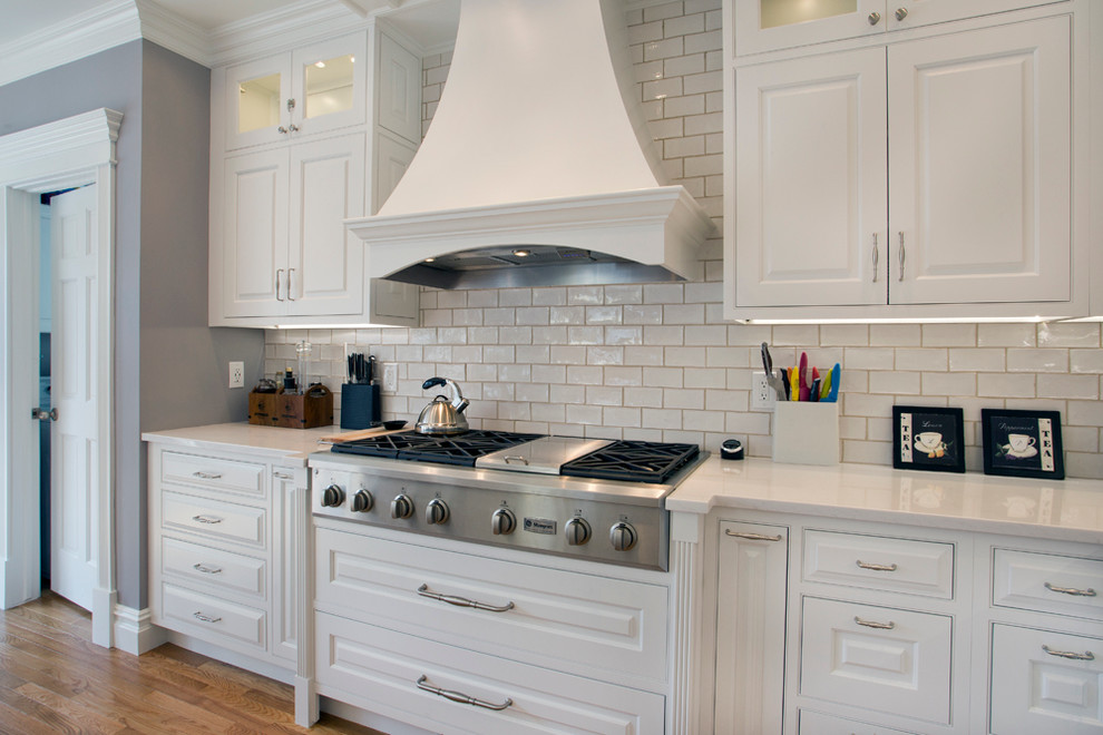 Eat-in kitchen - large transitional l-shaped medium tone wood floor eat-in kitchen idea with a farmhouse sink, white cabinets, granite countertops, white backsplash, stainless steel appliances, an island, raised-panel cabinets and subway tile backsplash