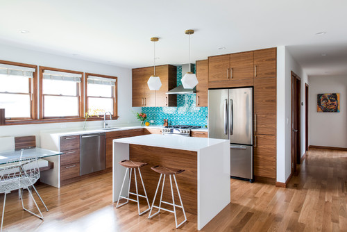 Modern kitchen with warm wood cabinets, white island, stainless steel appliances, and a blue tile backsplash, illustrating material and finish choices related to what are IKEA kitchen cabinets made of.