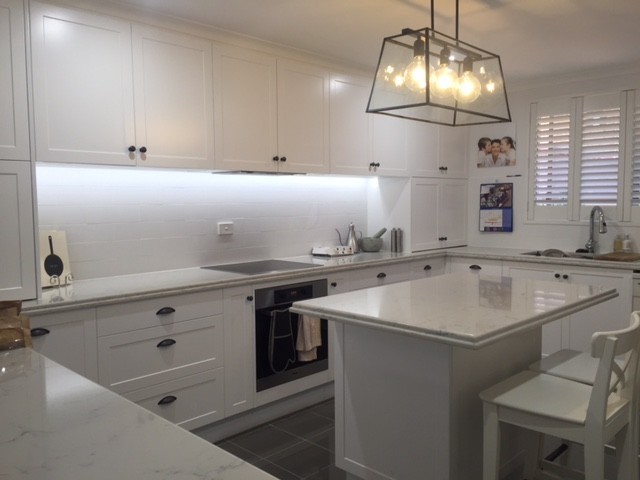 This is an example of a large transitional u-shaped eat-in kitchen in Brisbane with a double-bowl sink, raised-panel cabinets, white cabinets, quartz benchtops, white splashback, ceramic splashback, stainless steel appliances, porcelain floors and with island.