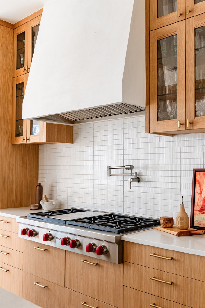 オースティンにあるトランジショナルスタイルのおしゃれなキッチン (フラットパネル扉のキャビネット、中間色木目調キャビネット、白いキッチンパネル、セラミックタイルのキッチンパネル、シルバーの調理設備、白いキッチンカウンター) の写真