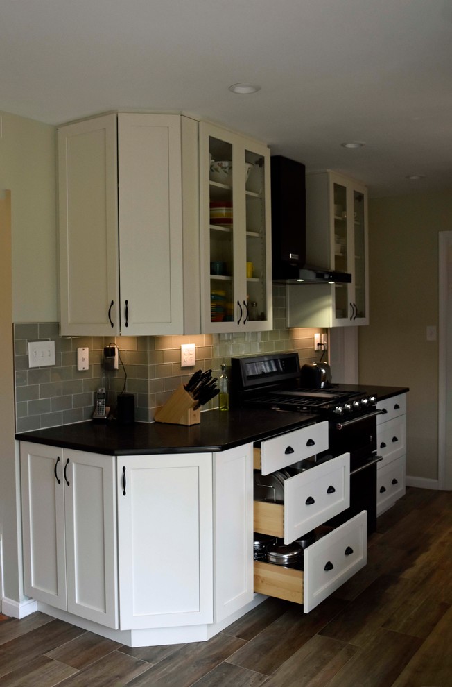 Mid-sized transitional galley laminate floor and brown floor enclosed kitchen photo in DC Metro with a farmhouse sink, shaker cabinets, white cabinets, granite countertops, gray backsplash, subway tile backsplash, stainless steel appliances, no island and black countertops