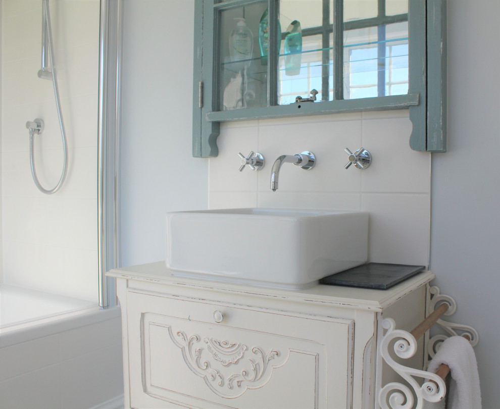 Photo of a mid-sized traditional master bathroom in Sussex with raised-panel cabinets, white cabinets, a drop-in tub, a shower/bathtub combo, a two-piece toilet, white tile, ceramic tile, blue walls, ceramic floors, a vessel sink, glass benchtops, blue floor, a hinged shower door, a single vanity and a freestanding vanity.