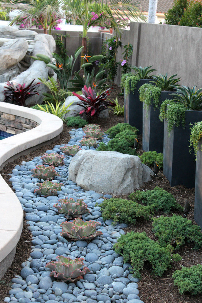 This is an example of a mid-sized mediterranean backyard full sun xeriscape for summer in Orange County with a water feature and natural stone pavers.