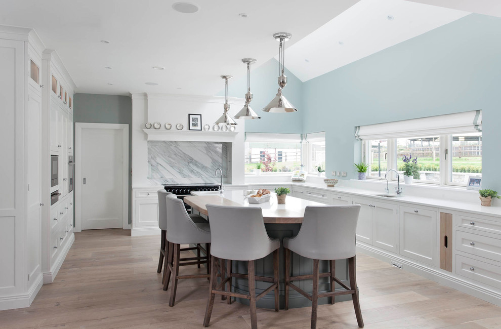 Design ideas for a large transitional l-shaped kitchen in Other with shaker cabinets, white cabinets, quartzite benchtops, marble splashback, black appliances, with island, white benchtop, an undermount sink, multi-coloured splashback, light hardwood floors and beige floor.