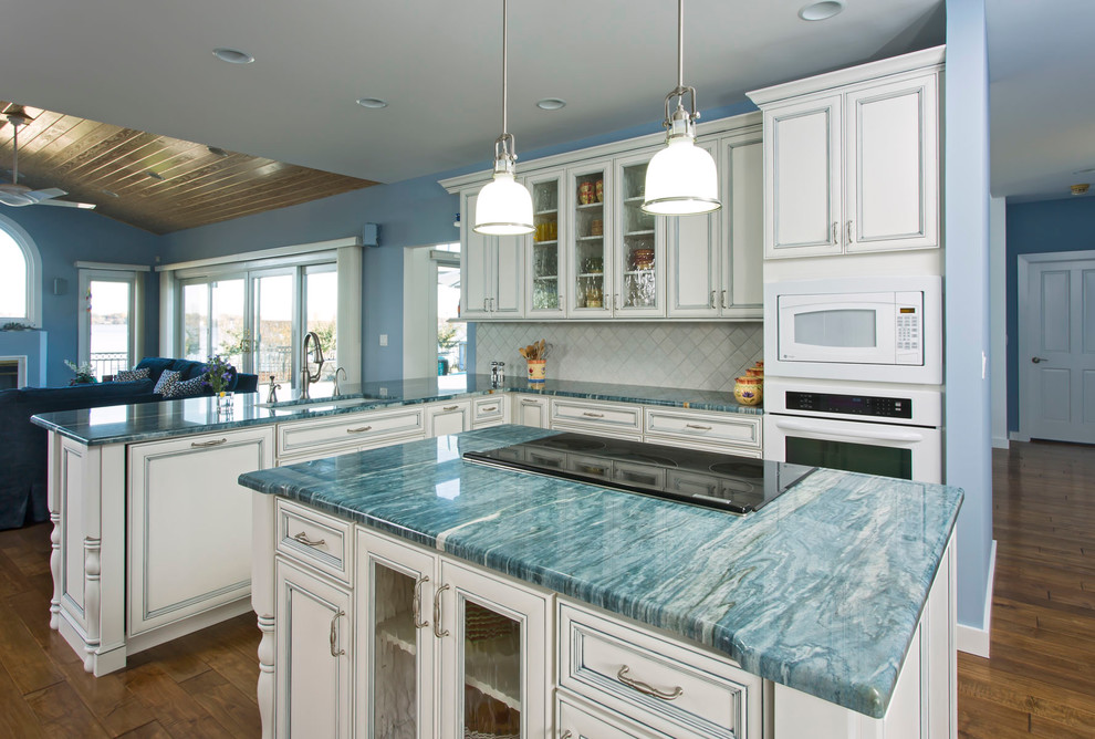 Design ideas for a mid-sized beach style l-shaped open plan kitchen in Charlotte with an undermount sink, with island, beaded inset cabinets, white cabinets, marble benchtops, white splashback, stone tile splashback, white appliances, medium hardwood floors and turquoise benchtop.