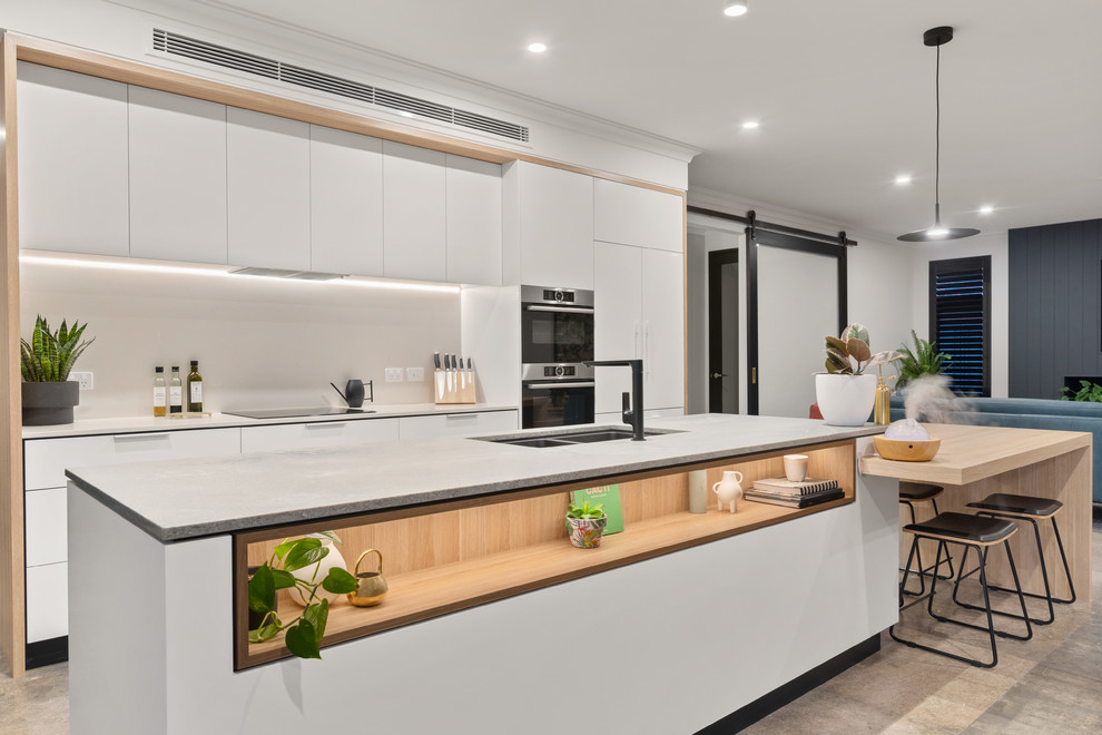 Design ideas for a contemporary open plan kitchen in Perth with a double-bowl sink, flat-panel cabinets, white cabinets, grey splashback, stainless steel appliances, with island, white benchtop and brown floor.