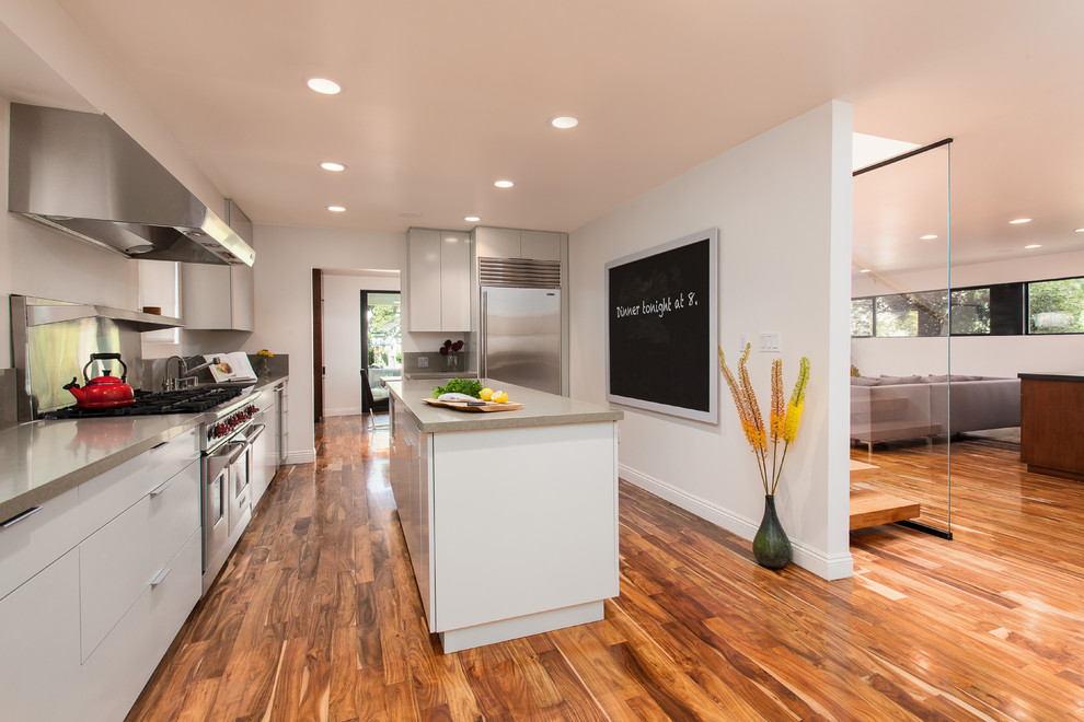 Large contemporary l-shaped separate kitchen in Los Angeles with flat-panel cabinets, white cabinets, grey splashback, stainless steel appliances, an undermount sink, quartz benchtops, stone slab splashback, medium hardwood floors, with island and brown floor.
