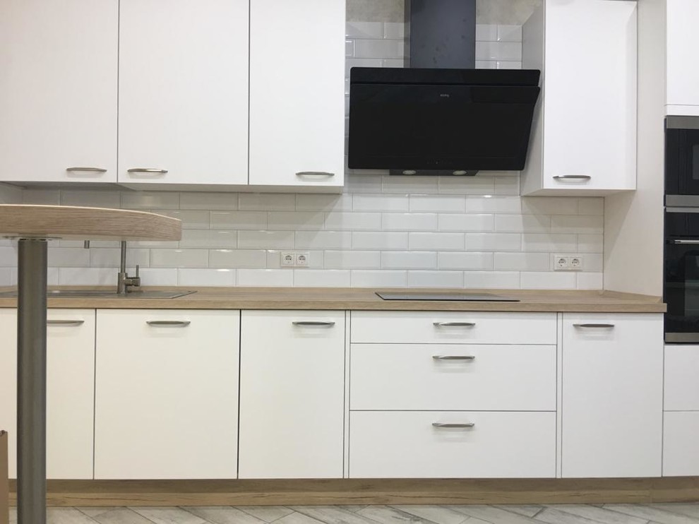 This is an example of a mid-sized scandinavian single-wall kitchen pantry in Other with a drop-in sink, flat-panel cabinets, white cabinets, laminate benchtops, white splashback, subway tile splashback, black appliances, porcelain floors, no island, grey floor and beige benchtop.