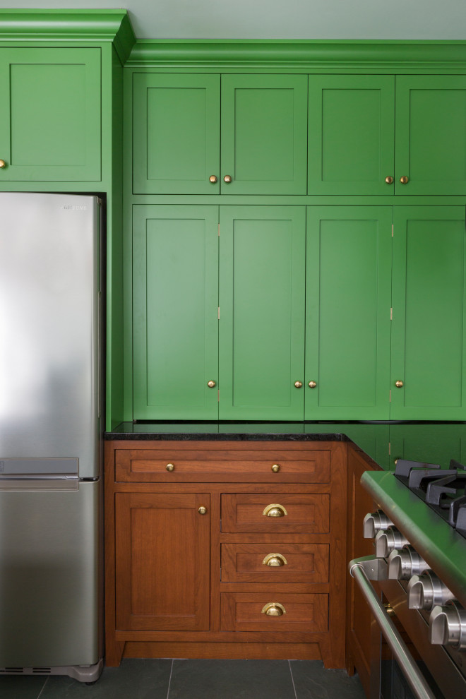 Inspiration for a mid-sized eclectic l-shaped eat-in kitchen in Philadelphia with an undermount sink, shaker cabinets, green cabinets, granite benchtops, white splashback, ceramic splashback, stainless steel appliances, slate floors, with island, green floor and black benchtop.