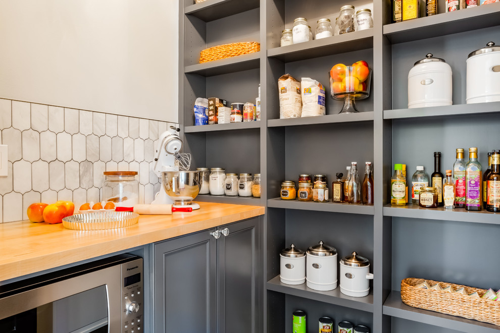 Photo of a mid-sized eclectic l-shaped kitchen pantry in Seattle with recessed-panel cabinets, grey cabinets, wood benchtops, white splashback, marble splashback, stainless steel appliances, no island and brown benchtop.