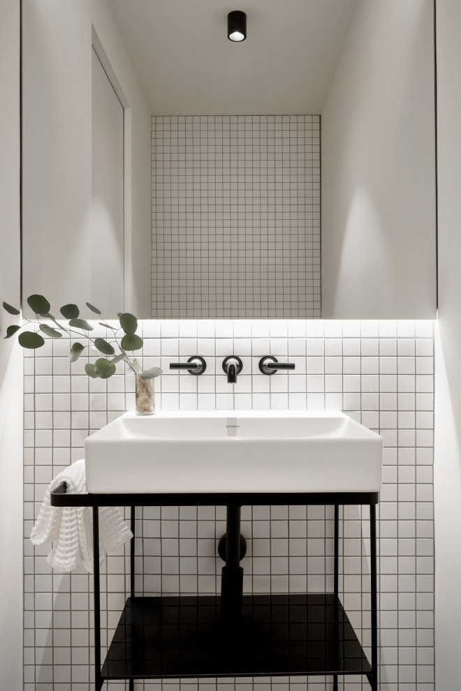 Bild på ett litet funkis vit vitt toalett, med öppna hyllor, vita skåp, en vägghängd toalettstol, vit kakel, porslinskakel, vita väggar, travertin golv, ett piedestal handfat och grått golv