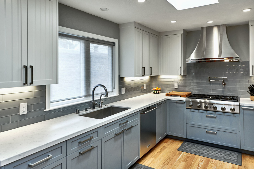 Mid-sized transitional u-shaped open plan kitchen in San Francisco with an undermount sink, louvered cabinets, blue cabinets, marble benchtops, grey splashback, glass tile splashback, stainless steel appliances, medium hardwood floors, no island, brown floor and white benchtop.
