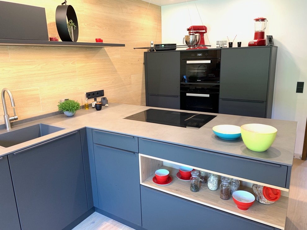 Mittelgroße Industrial Wohnküche in L-Form mit integriertem Waschbecken, flächenbündigen Schrankfronten, Rückwand aus Keramikfliesen, schwarzen Elektrogeräten und Halbinsel in Sonstige