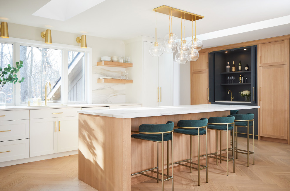 This is an example of a large contemporary l-shaped kitchen/diner in Grand Rapids with a submerged sink, shaker cabinets, light wood cabinets, white splashback, porcelain splashback, integrated appliances, light hardwood flooring, an island and white worktops.