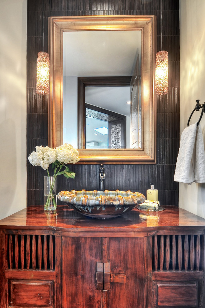 Inspiration for a small tropical powder room in Los Angeles with a vessel sink, furniture-like cabinets, dark wood cabinets, wood benchtops, brown tile, black walls and brown benchtops.