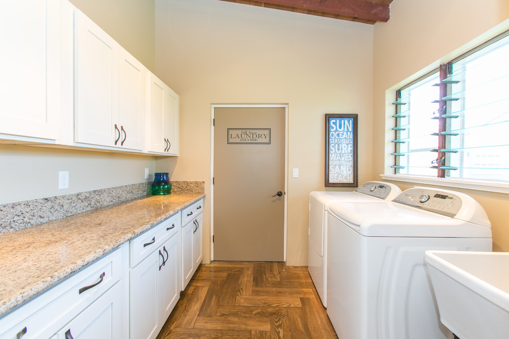 Inspiration for a mid-sized beach style galley utility room in Hawaii with an utility sink, shaker cabinets, white cabinets, granite benchtops, beige walls, dark hardwood floors, a side-by-side washer and dryer, brown floor and beige benchtop.