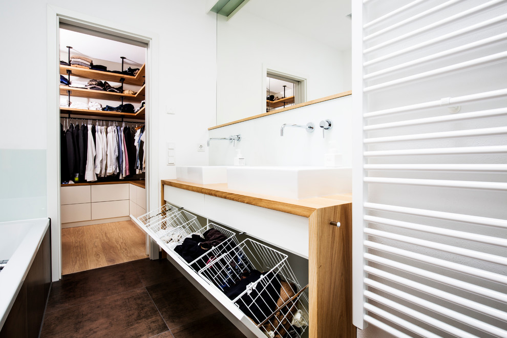 Badezimmer En Suite With weißer Wandfarbe, flächenbündigen Schrankfronten, weißen Schränken, Einbaubadewanne, bodengleicher Dusche, Wandtoilette, weißen Fliesen, Porzellanfliesen, Zementfliesen für Boden, Aufsatzwaschbecken, Waschtisch aus Holz, braunem Boden, offener Dusche and brauner Waschtischplatte in Munich