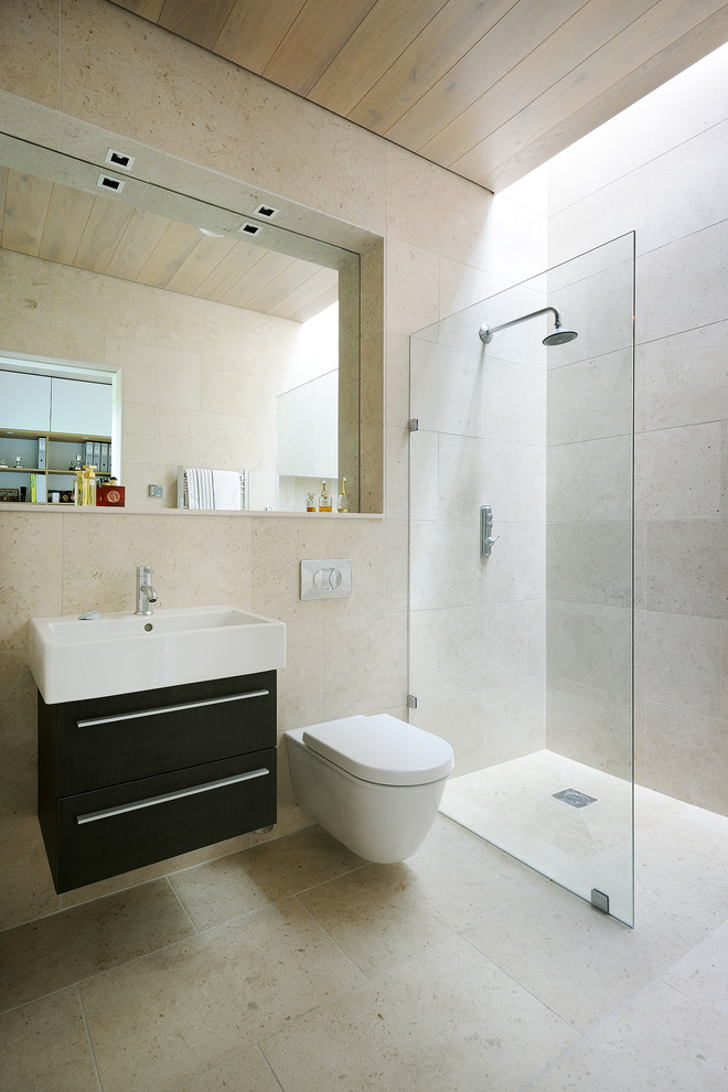 This is an example of a contemporary bathroom in Hampshire with a wall-mount sink, dark wood cabinets, marble benchtops, an open shower, a wall-mount toilet, beige tile, beige walls and an open shower.