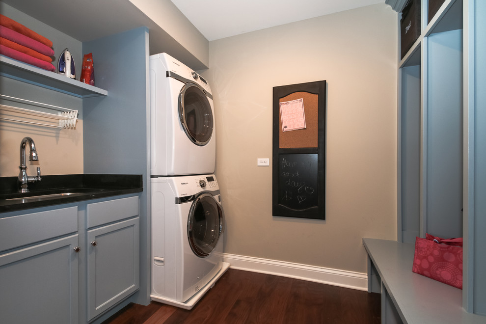 Inspiration for a traditional galley utility room in Chicago with an undermount sink, shaker cabinets, blue cabinets, granite benchtops, beige walls, dark hardwood floors and a stacked washer and dryer.