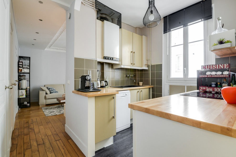 This is an example of a contemporary galley kitchen in Paris with a drop-in sink, flat-panel cabinets, green cabinets, green splashback, white appliances, grey floor and brown benchtop.