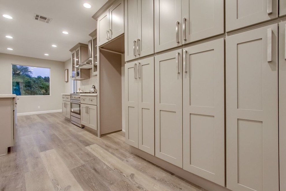 Photo of a large transitional single-wall eat-in kitchen in Los Angeles with a farmhouse sink, shaker cabinets, grey cabinets, quartz benchtops, brown splashback, mosaic tile splashback, stainless steel appliances, dark hardwood floors and with island.